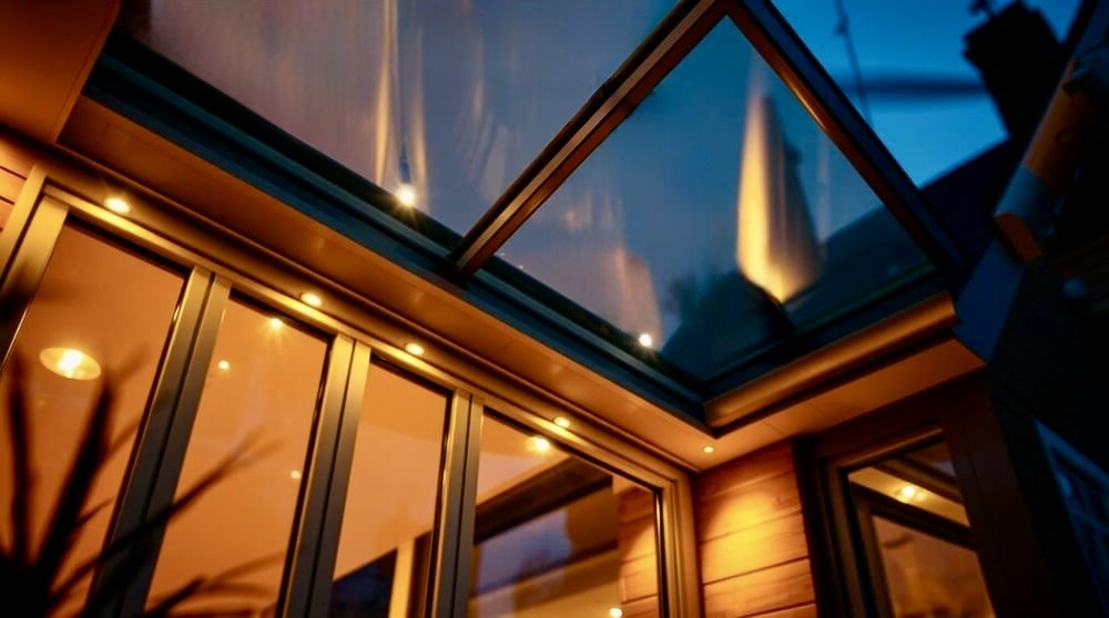 Illuminated modern roof lantern with slim aluminium frames on a flat roof extension at dusk, showcasing ambient lighting and reflective glass. This image demonstrates how roof lanterns bring natural light into contemporary living spaces, aligning with content focused on home improvement solutions.